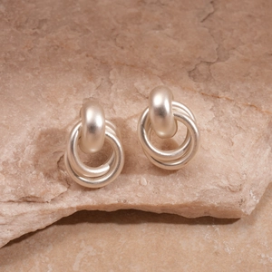 Vue macro des boucles d'oreilles anneaux entrelacés argent mat sur une surface en pierre