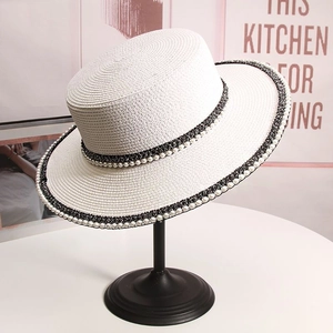 Detail of white boater straw hat featuring a black ribbon band and elegant pearl accents