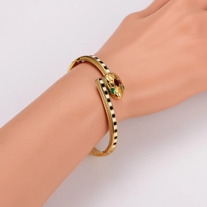 Golden snake-shaped bangle with black and white enamel scales and green eye details