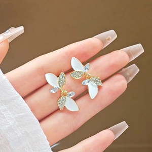 Elegant gold leaf earrings with white enamel and sparkling rhinestones shown on hand