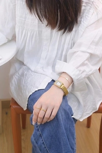 Close-up of golden rectangular Roman watch with matching wavy rings and heart bracelet