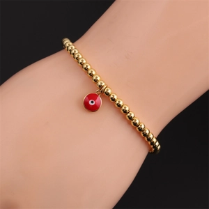 Detail of gold beaded elastic bracelet with red enamel evil eye charm on wrist