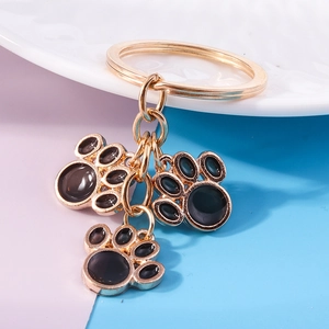 Detail of three black enamel cat paw charms on a golden metal keychain ring accessory