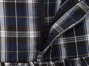 Detailaufnahme des schwarzen Reißverschlusses auf dem blau-weißen Karo-Midikleid-Stoff