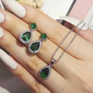 Close-up of emerald drop necklace and earrings set worn on hand with white nails