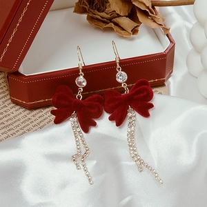 Detail of red velvet bow earrings with silver needles and dangling rhinestone tassels