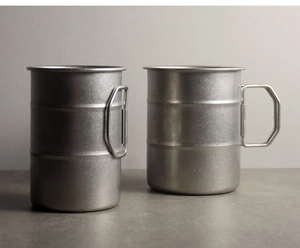 Detail of two portable stainless steel camping cups with space-saving folding handles
