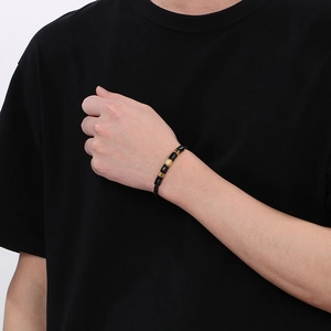 Close-up of a men's black woven leather bracelet featuring detailed gold metal hardware