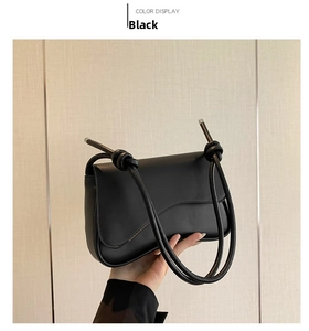 Detail of minimalist black crossbody bag showing knotted strap and flap closure design