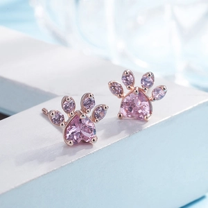 Macro detail of rose gold paw-shaped earrings with pink heart-shaped stones