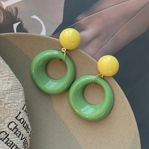 Gros plan de boucles d'oreilles créoles bicolores en acrylique jaune et vert sur plateau