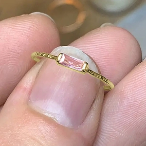 Close-up of a minimalist gold ring featuring a hammered texture and rectangular pink stone
