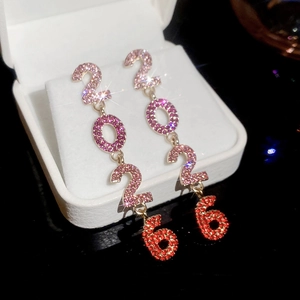 Gros plan de boucles d'oreilles pendantes avec chiffres 2026 en cristal rose étincelant sur boîte