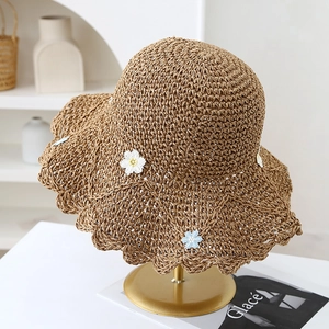 Detail of hand-woven straw hat with daisy flowers and wavy brim on gold display stand