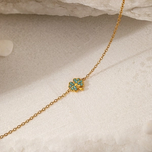Makroaufnahme von vergoldetem Edelstahlarmband mit blauem Strass-Vierklee-Anhänger