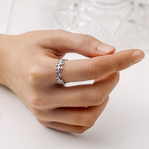 Detailed close-up of a silver vine leaf ring worn on index finger with a soft background