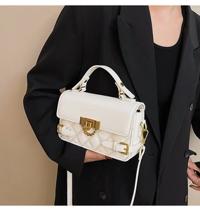 Detail of white quilted handbag with gold hardware, chain decor, and top handle