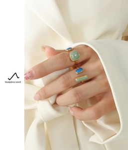 Detail of four gold-plated stainless steel rings with colorful enamel on a hand