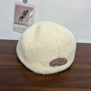 Detail shot of a knit beret featuring a signature silver metal logo and soft wool texture