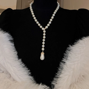 Close-up of elegant Y-shaped pearl necklace with golden teardrop pendant on model