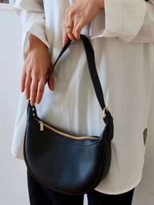 Detail of black crescent saddle bag with gold hardware worn on model for size perspective