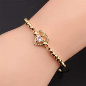 Detail of adjustable gold beaded bracelet featuring a sparkling zircon heart charm on wrist