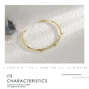 Close-up of gold-plated open bangle featuring three sparkling zircons on a white surface