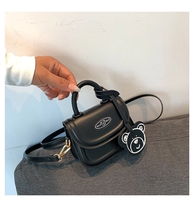 Mini black PU leather handbag with a bear charm, held to show its compact size