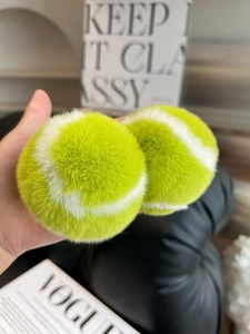 Close-up of bright green faux fur tennis ball keychains held by hand over a magazine