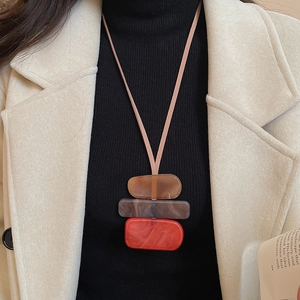 Close-up of a geometric acrylic pendant necklace in orange, clear grey, and coffee tones