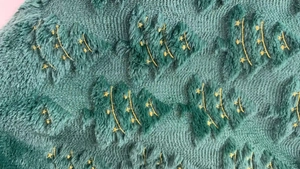 Close-up of a green plush fabric featuring an embroidered gold star Christmas tree pattern