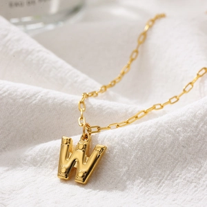 Macro shot of 18K gold letter W pendant with bubble texture on rectangular link chain