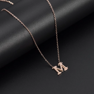 Rose gold letter M pendant necklace with delicate chain shown on a dark background