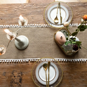 Detailed tabletop layout featuring a jute table runner with pompom fringe and gold cutlery