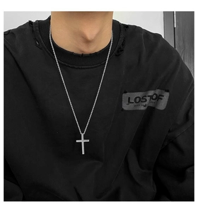 Close-up of a silver cross pendant necklace worn by a male model over a black hoodie