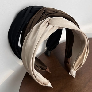 Detailed view of twisted satin headbands in black, dark brown, and beige on wooden surface