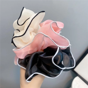 Close-up of three layered chiffon scrunchies in white, pink, and black with contrast edging