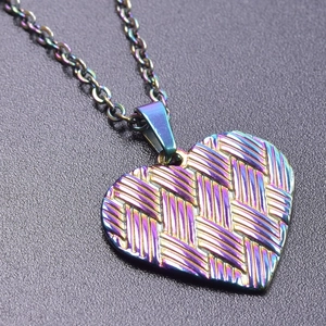 Detail of heart-shaped stainless steel pendant with woven texture and rainbow finish