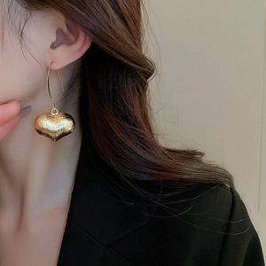Macro shot of gold heart-shaped earrings with a brushed metal texture worn by a model