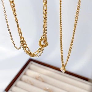 Detailed view of layered gold necklaces with teardrop zircon and snake chain texture