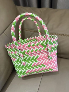 Detail of pink, green and white woven basket bag on brown leather background