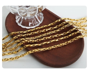 Macro view of gold-plated twisted rope chain necklaces on a dark wooden tray