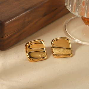Macro shot of 18k gold plated irregular square earrings on soft beige linen fabric