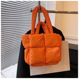 Detail of a bright orange padded quilted tote bag hanging in a minimalist urban setting