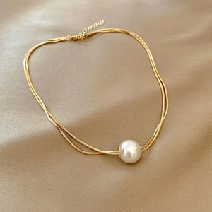 Elegant gold double-layer titanium necklace with a white pearl pendant on silk fabric