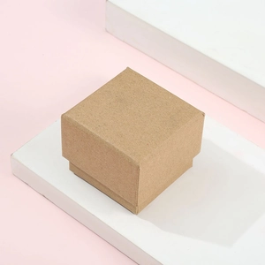 Macro shot of square kraft paper jewelry box on a white pedestal with soft pink background