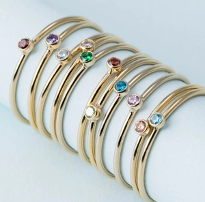Close-up of minimalist thin gold rings set with various colored round gemstones