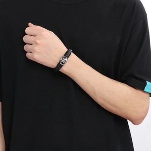Close-up of a black braided leather bracelet with a silver skull detail on a male wrist