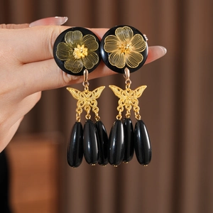 Detail of vintage earrings with gold flower motif, butterfly and black teardrop tassels
