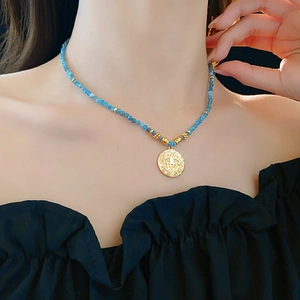 Detail of ethnic beaded necklace with blue beads and a gold evil eye pendant on model